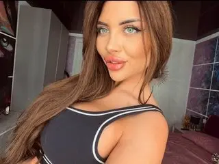 MoniqueCeleste poses with long brown hair, wearing a black tank top with white trim, looking directly at the camera.