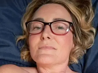 MsGee wearing glasses and looking into the camera while lying on a blue pillow.