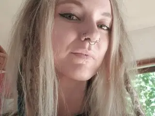 Close-up portrait of a blonde woman with nose piercings and winged eyeliner looking thoughtfully at the camera.