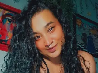 Smiling woman with long curly dark hair in a cozy room with colorful framed art on the wall.
