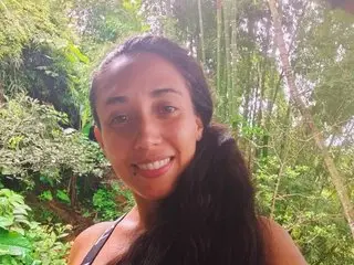 Smiling woman in casual summer attire enjoying a peaceful moment in a lush, sunlit tropical forest.