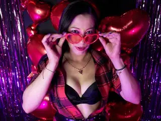 NahomiPeppers poses in a red plaid shirt and black bra, showing her long dark hair and cleavage against a purple background.