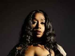 NaliniWestwood poses with long wavy black hair and a dark choker against a black background.