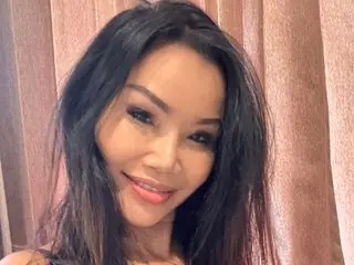 Namfa smiling at the camera with long dark hair in front of pink curtains.