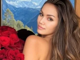 Namfa poses with long brown hair looking over her shoulder next to a bouquet of red roses.