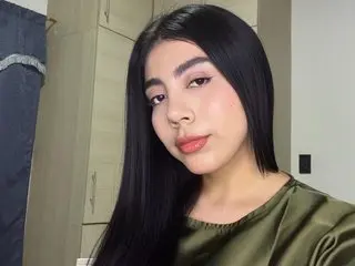 Nanabellatop with long black hair wearing a dark green satin top, posing and looking directly at the camera.