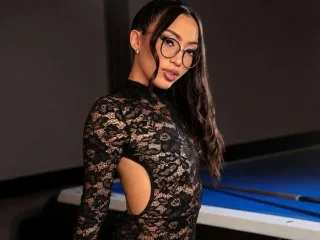 NaomiBendz wears a black lace long-sleeve bodysuit with side cutouts while posing in a game room near a blue pool table.