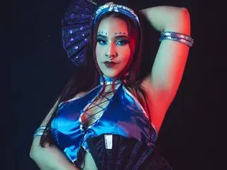 NaomyEvanss poses in a blue shiny top and headpiece, showing her face and shoulders against a dark background.