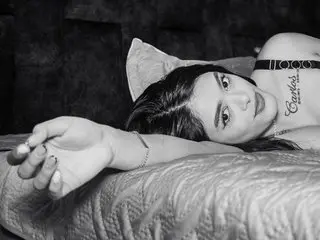 Natasha_Angell lying back with her dark hair spread out, wearing a black bra and showing her neck and collarbone.