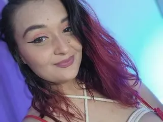 Smiling woman with reddish-purple hair wearing a white crisscross top against a blue background.