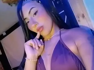 Young woman in a dark halter top and gold necklace posing with a moody expression in dim blue lighting.
