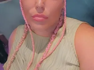 Naughty_Laurenx poses close up, showing her face and pink braided hair while wearing a light green sleeveless top.