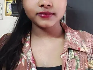 Naughtyriya — Naughtyriya looks at the camera with long dark hair, wearing a pink floral patterned shirt or blouse.