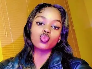 Young woman with winged eyeliner and black leather jacket making a playful expression in front of gold blinds.