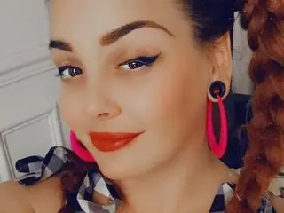 Nectarxmagic poses close-up with dark hair and red lipstick, wearing large pink hoop earrings and a black and white patterned top.