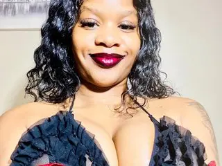 Neeshaa smiles while wearing a black ruffled bikini top that shows off her cleavage and dark, wavy hair.