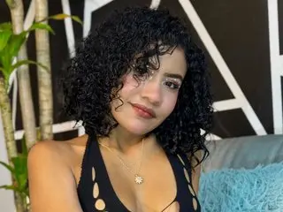 NeytiriRoss poses with her curly dark hair, wearing a black low-cut top that shows her cleavage and shoulders.