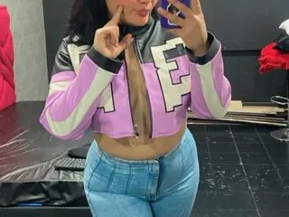 Woman in a trendy lilac and black cropped jacket and blue jeans posing in a casual indoor setting.