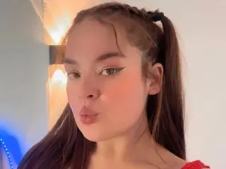 Nikkinovacs poses with a pouty expression, showing her long brown hair styled in pigtails against a plain wall background.