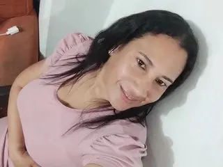 NinaSimonne smiles while posing close up, showing her dark hair and pink top against a plain white wall.