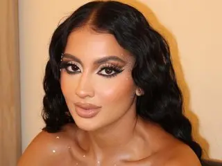 Glamorous woman with wavy black hair and dramatic smoky eye makeup looking elegant in a soft-lit setting.