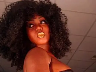 NiotMoreaux poses with her dark curly hair and mouth open, showing her teeth and tongue while looking toward the camera.