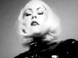 Glamorous blonde woman in a black latex outfit posing with a moody, cinematic aesthetic.