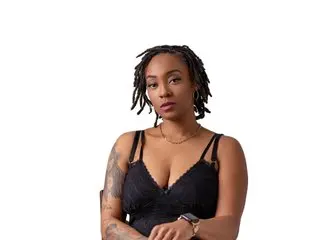 NovaLuxe26 poses in a black lace bra, showing her dark hair and tattoos against a plain white background.