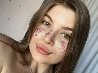 NylonMuse smiles with glittery pink heart-shaped sparkles on her cheeks and nose, showing her long brown hair and clear skin.