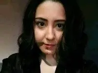 OfSexyWoman poses with long dark hair and a direct gaze, wearing a black top against a dark background.