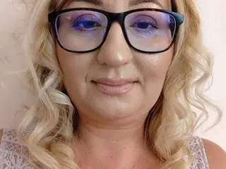 OlgaPavllova, a blonde woman, looks directly at the camera wearing black-rimmed glasses in a close-up headshot.
