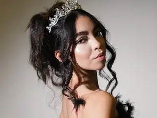 OliviaPagani poses with her dark wavy hair styled up, wearing a silver tiara against a plain light background.