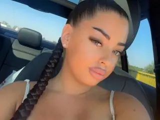 Young woman with long dark braid in a white tank top sitting in a convertible car on a sunny day.