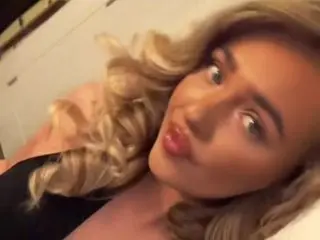OneandonlyKate poses close-up, showing her blonde wavy hair and face while wearing a black top.