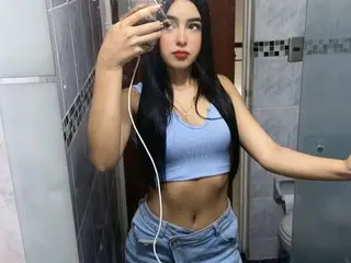 Only_dolls poses in a blue crop top and denim shorts, showing her midriff and long dark hair in a bathroom setting.