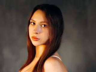PaigePrado looking at the camera with long dark hair against a dark background.