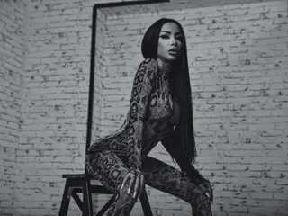 Glamorous woman in a snakeskin print bodysuit posing against a white brick wall in a moody studio setting.