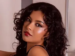 Glamorous woman with curly dark hair and red lipstick posing in a black outfit with a moody aesthetic.