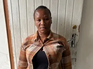 Peachesx25 poses looking at the camera wearing a brown plaid button-down shirt against a white slatted door background.
