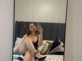 Young woman in black lace lingerie and devil horns sitting on a bed in a modern bedroom.