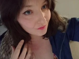 PeachyXXXX — PeachyXXXX looks toward the camera with a soft expression, her dark hair framing her face against a plain background.