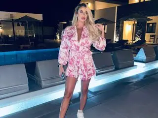 PearlPlenty poses outdoors at night wearing a pink and white patterned wrap dress that shows off her legs and cleavage.