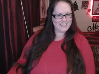 Smiling woman with long dark hair wearing a red sweater in a cozy indoor setting.