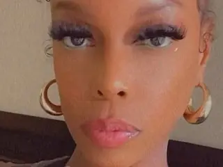PerkyBabe looks directly at the camera with long eyelashes and gold hoop earrings, showing her face and neck.