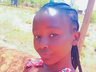 Young girl with braided hair wearing a pink floral top in a sunny outdoor rural setting.