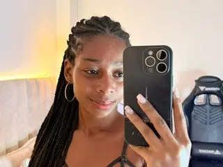 PixzyMartinez poses for a mirror selfie, showing her long dark braids and a black bra or top against a plain background.