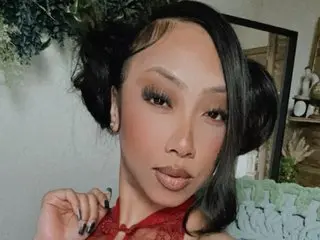 PreeminentJesss poses close-up, showing her face, dark hair, and red lace top against a soft indoor background.
