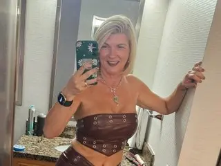 Prettypetunia52 smiles while wearing a brown leather bra and posing in a bathroom setting.