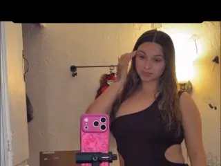 Princess1234 poses with her long dark hair down, wearing a black tank top while looking into the camera in a room setting.
