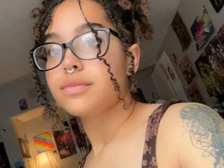 PrincessAriesRose wears black-rimmed glasses and looks forward with her curly hair styled in dreadlocks.